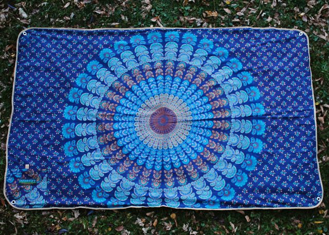 Blue mandala-patterned tapestry on grass background.