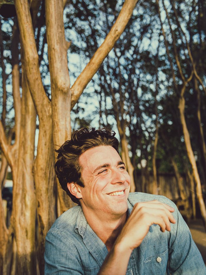 Smiling man outdoors near tall trees.