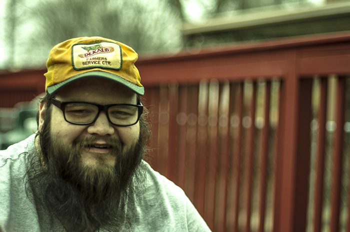 Man smiling, wearing yellow hat and glasses.