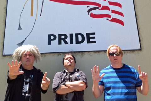 Three men posing under a pride sign.
