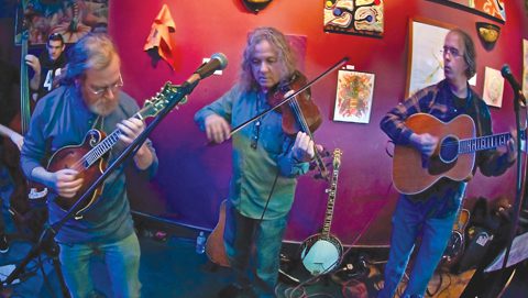 Three musicians performing with string instruments indoors.