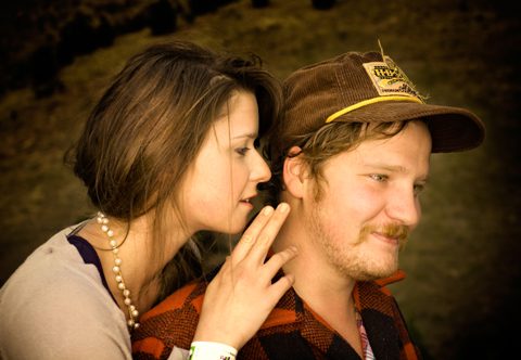 Woman whispering to man wearing a cap.