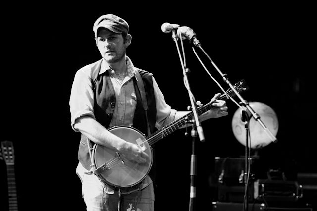Musician playing banjo on stage, black and white.