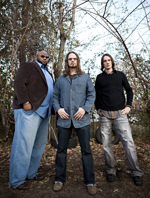 Three men standing in a wooded area.
