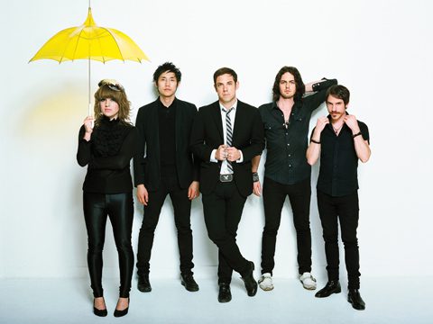 Five people posing with a yellow umbrella.