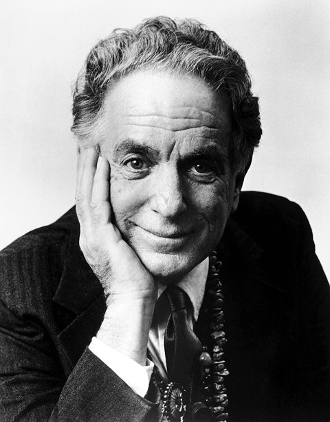 Elderly man smiling with hand on face.