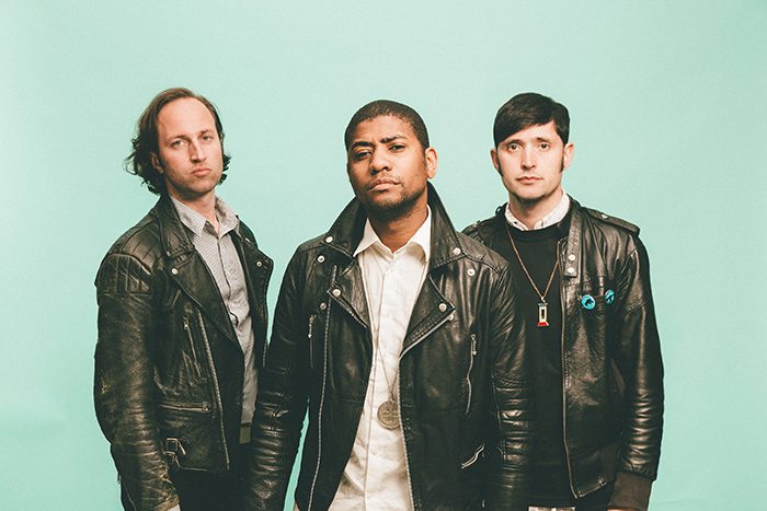 Three men wearing leather jackets, serious expressions.