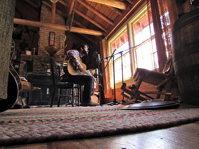 Musician playing guitar in rustic cabin.