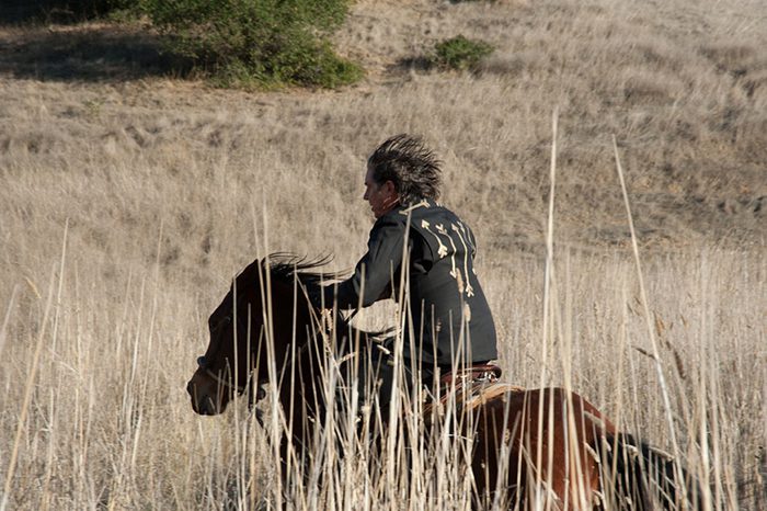 Person riding horse through dry grassland.