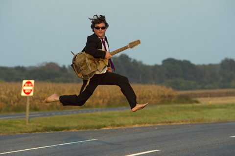 Man in suit jumping with a guitar.