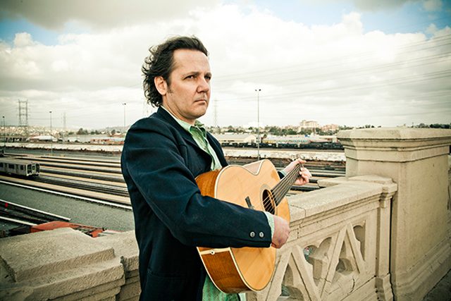 Man holding guitar on a bridge.