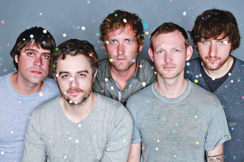 Five men with confetti, serious expressions.