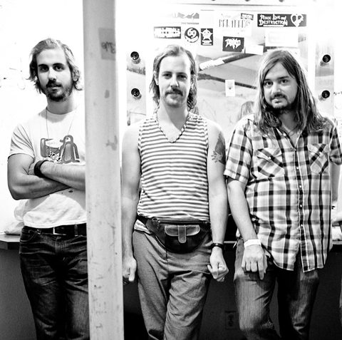 Three men standing in a dressing room.