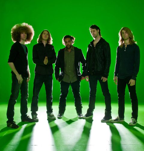 Five people standing against a green background.