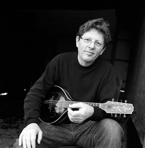 Man with mandolin sitting in dark room.
