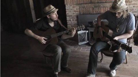 Two musicians playing acoustic guitars indoors.