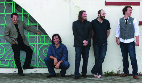 Five men standing and smiling against wall.