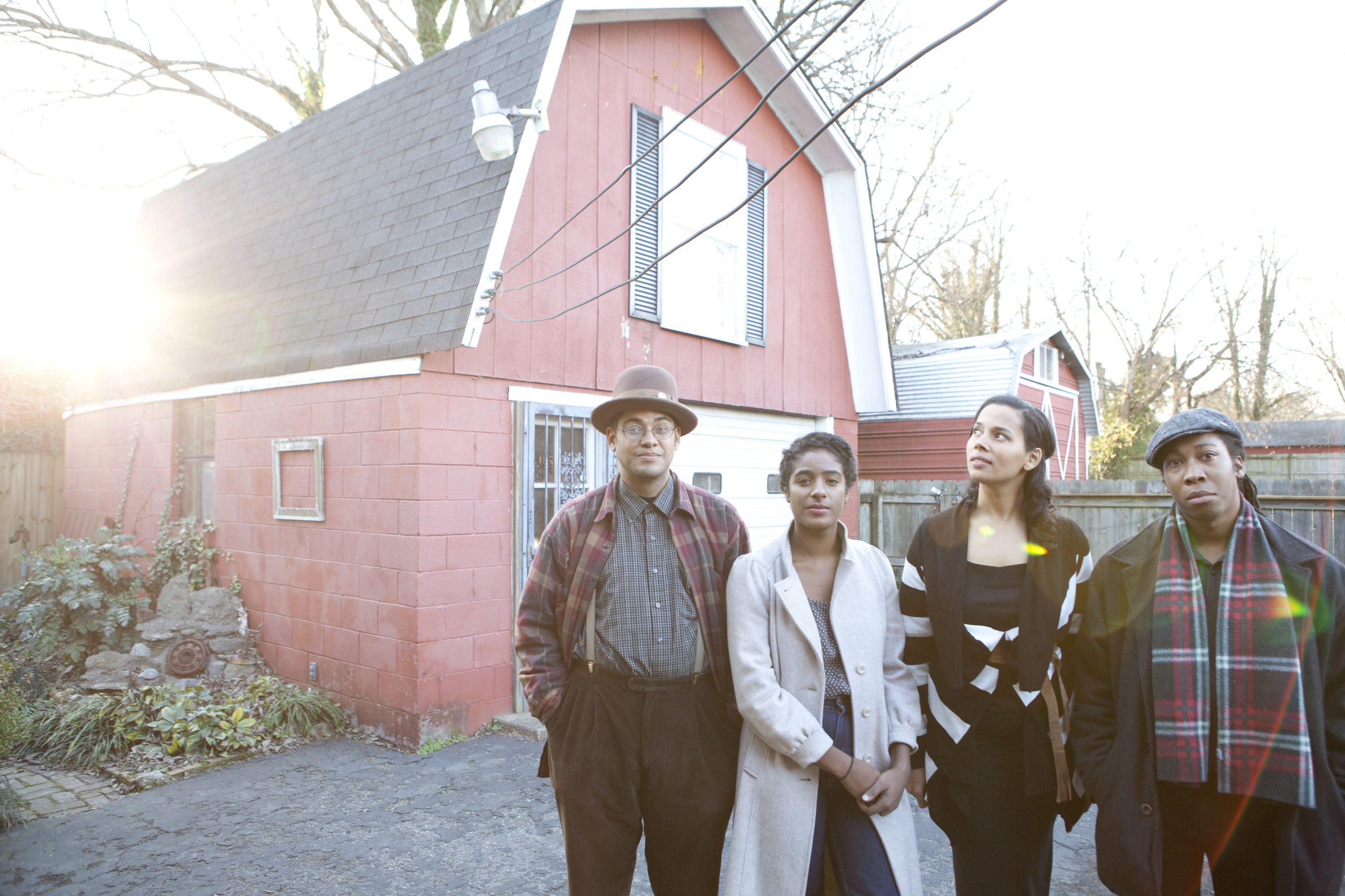 Four people standing outside red house.