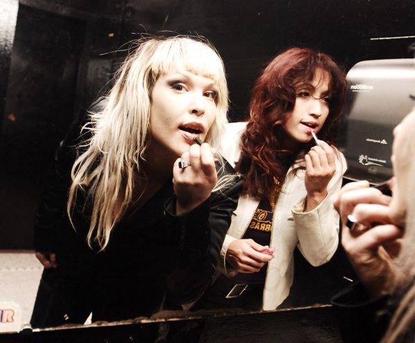Two women applying makeup in mirror.