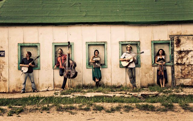 Five musicians standing with instruments in windows.