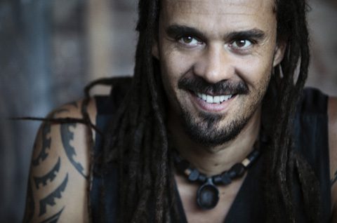 Smiling man with dreadlocks and tattoos.