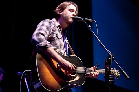 Singer playing guitar on stage with microphone.