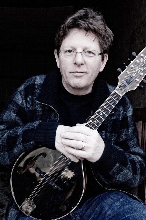 Man holding a mandolin, wearing glasses.