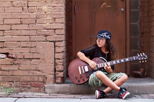 Child playing guitar on urban street.