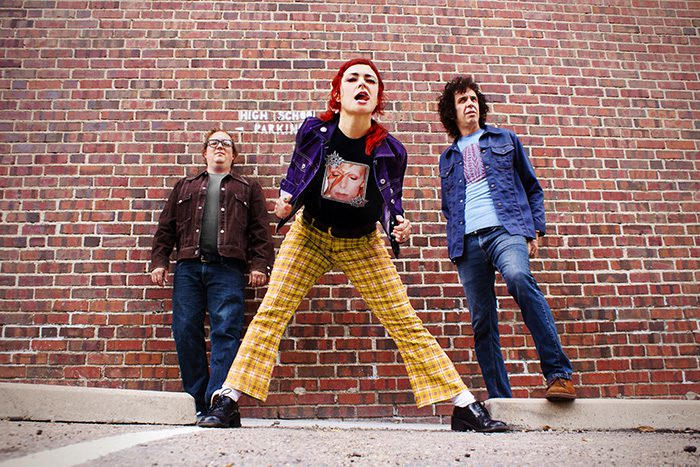 Three people posing against brick wall.