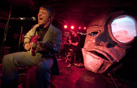 Musician performing on stage with large mask.