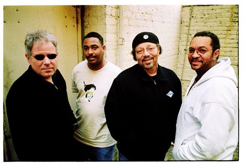 Four men standing against a brick wall.