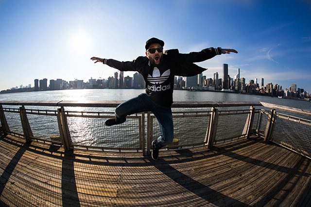Man jumping on pier, cityscape in background.