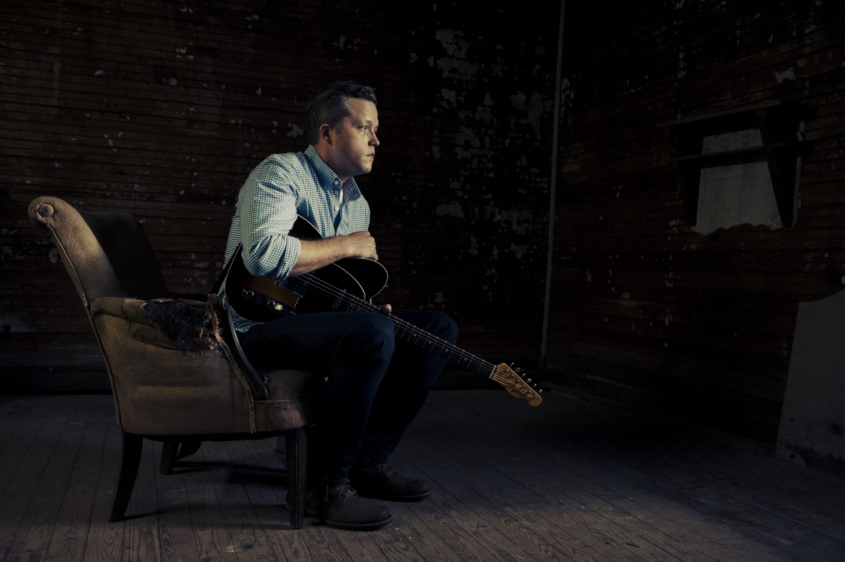 Man sitting with guitar in dimly lit room.