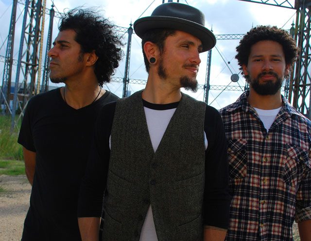 Three men standing outdoors near metal structures.