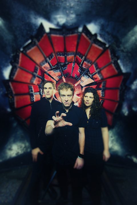 Three people posing in front of artwork.