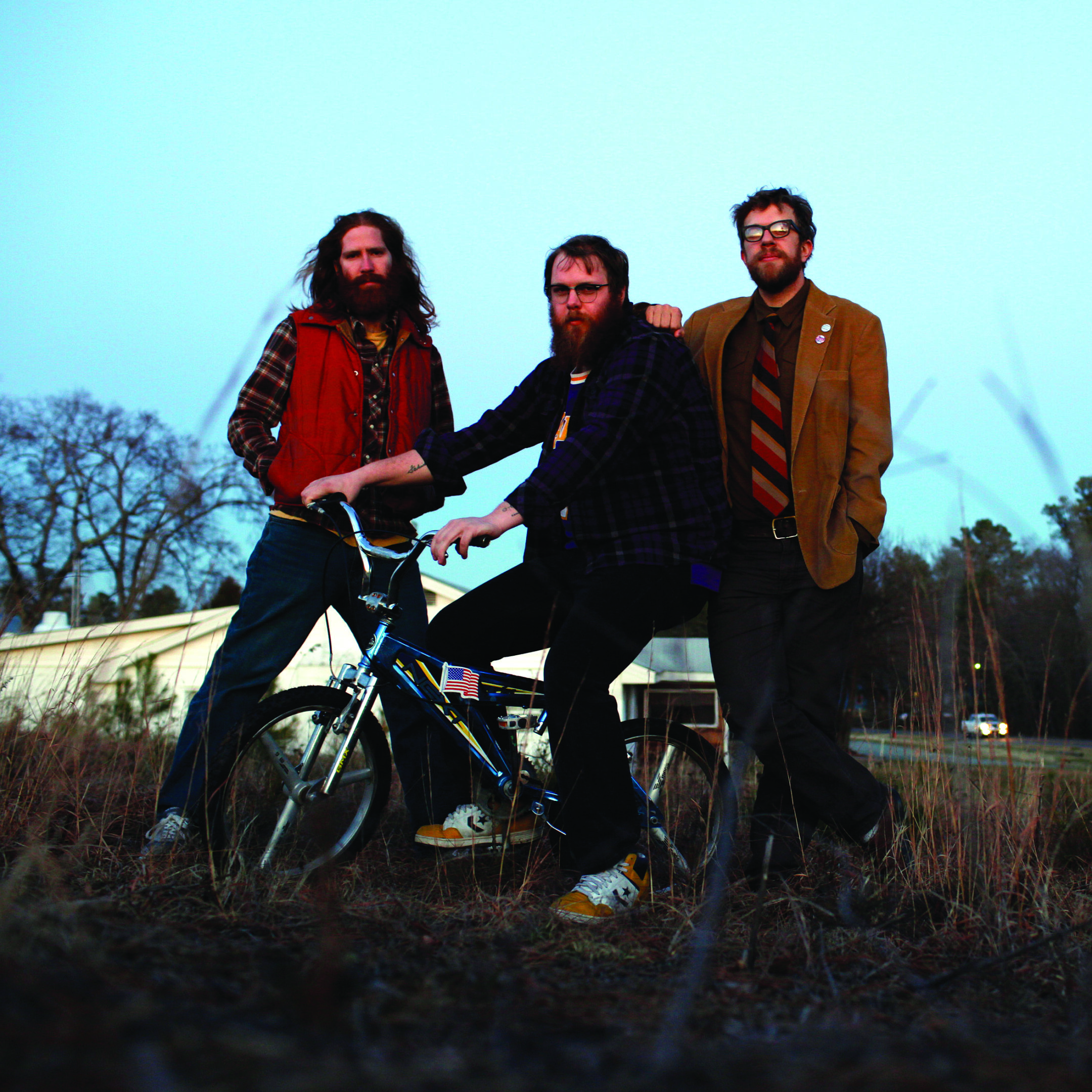 Three men with bicycle in rural setting.