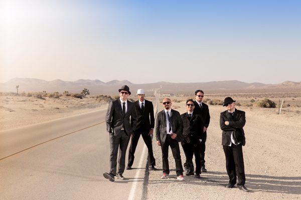Band posing on desert road in suits.