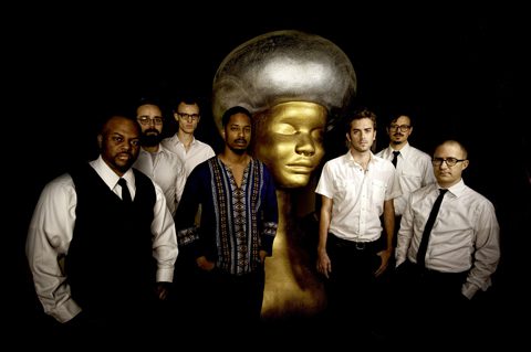 Seven men posing with large golden sculpture.