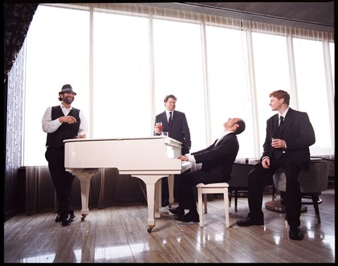 Four men gathered around a white piano.