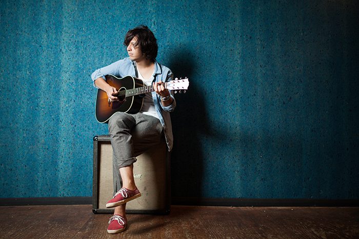 Person playing guitar on amplifier, blue background.