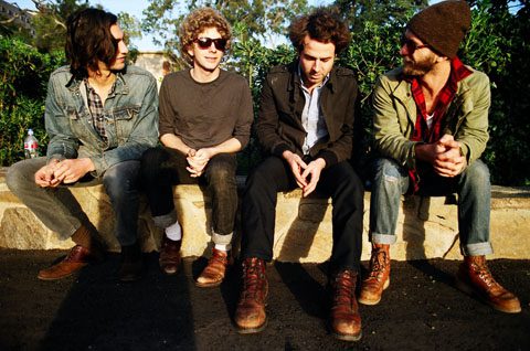 Four men sitting on a stone wall.