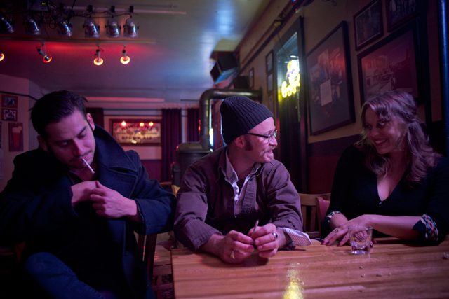 Three people conversing at a dimly lit bar.