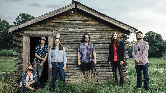 Six people in front of rustic cabin.