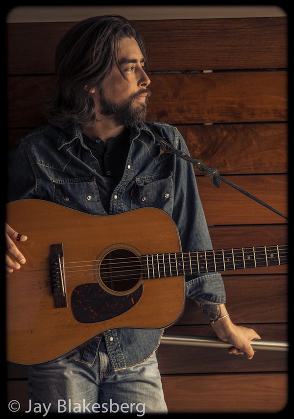 Man holding acoustic guitar, looking sideways.