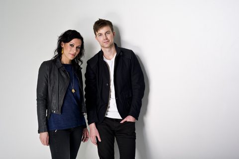 Man and woman standing against white wall.