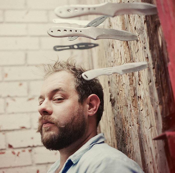 Man with knives stuck in wooden wall.