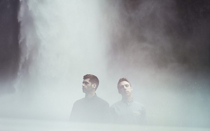 Two men standing near a misty waterfall.