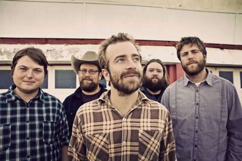 Five men standing in plaid shirts outdoors.
