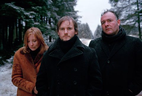 Three people standing in snowy forest.