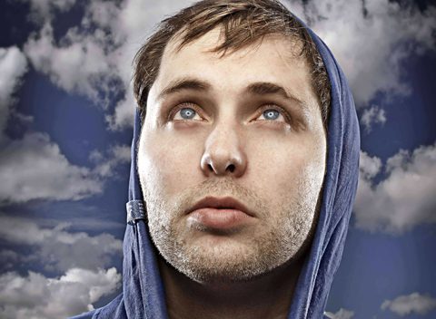Man in hoodie gazing at cloudy sky.